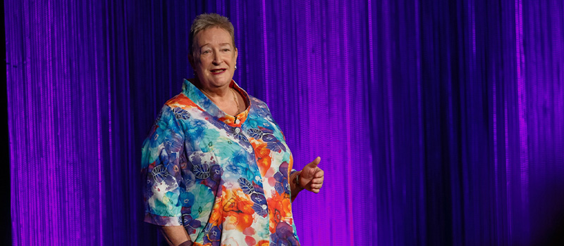 Sue Fraser is shown on stage, in front of a purple backdrop