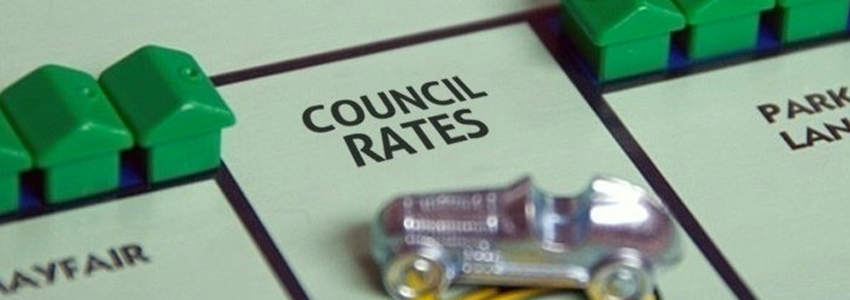 A photograph of a Monopoly board square that reads "COUNCIL RATES". A Monopoly car figurine and other surrounding squares are out of focus around it.