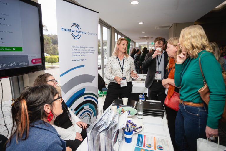 A group of people gathered around the ESC stand at the FCVic 2023 Conference. They are animated in conversation.