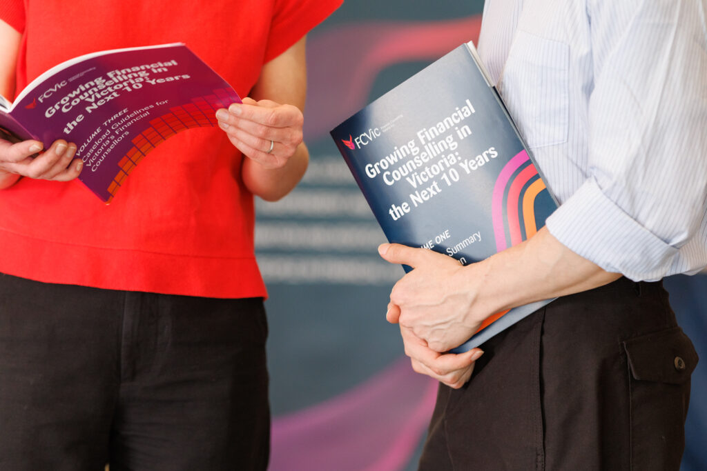Cropped photo of two people holding and reading the Growing Financial Counselling in Victoria Reports