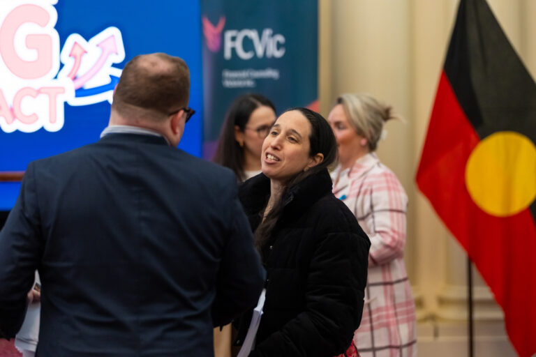 An attendee speaks with a man near the FCVic banner and Aboriginal flag on stage.