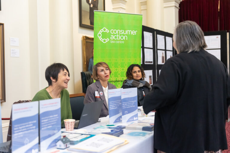 Three representatives from the Consumer Action Law Centre speak with a visitor at their exhibition booth.