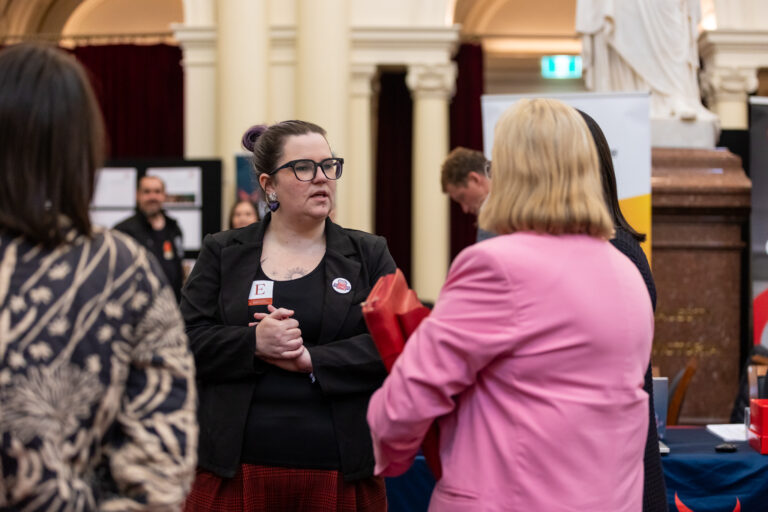An attendee speaks with two others near a statue and exhibition banners in Queens Hall.
