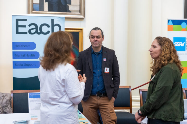 Three attendees speak near the EACH and Social Security Rights Victoria exhibition banners.