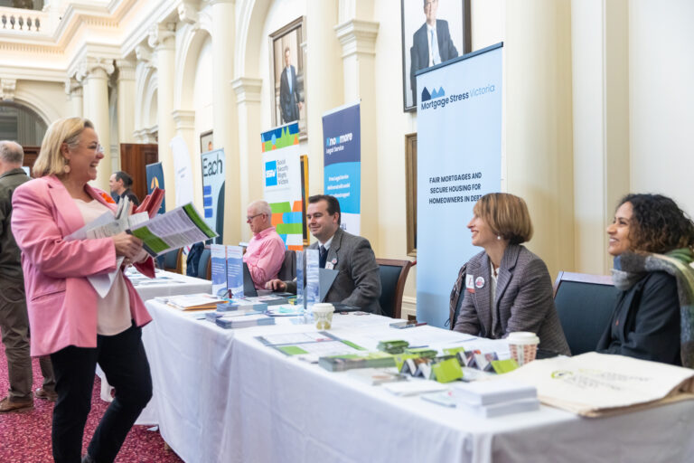 A visitor greets representatives from EACH, Social Security Rights Victoria, Knowmore Legal Service and Mortgage Stress Victoria at their exhibition tables.