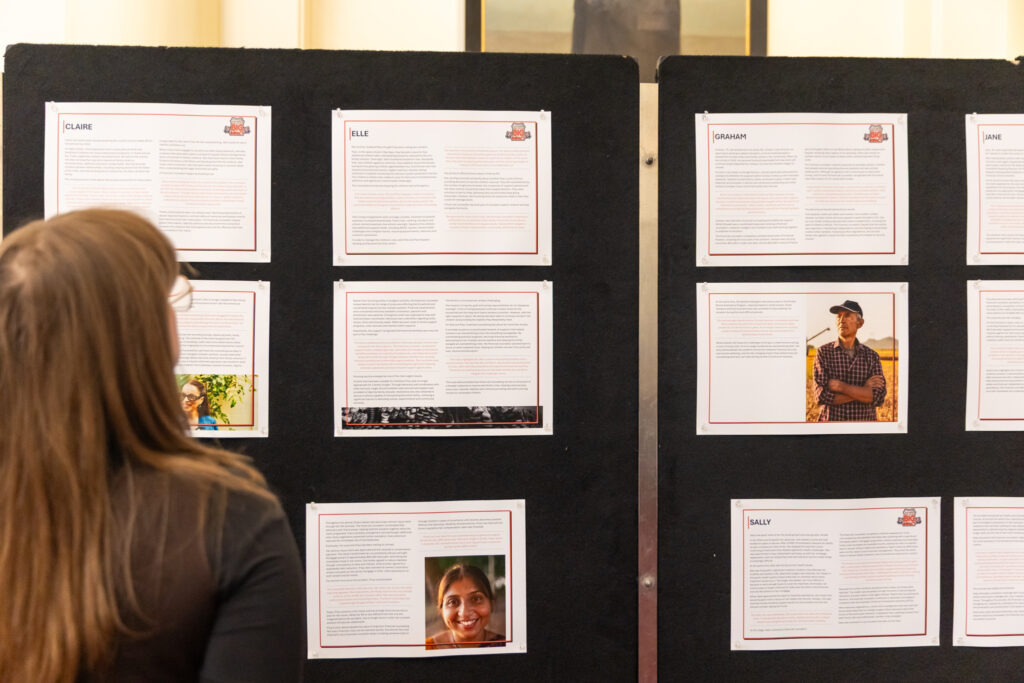 A visitor reviews case study panels at the exhibition, with client photos and stories displayed on black display boards.