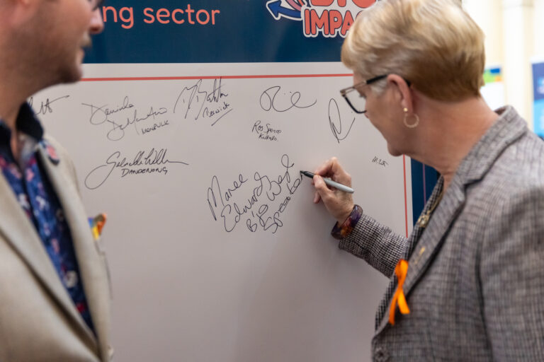 Maree Edwards MP, Speaker of the Victorian Legislative Assembly, signs the pledge wall as an FCVic representative looks on.