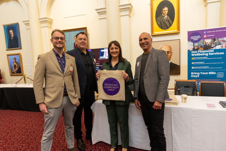 Rachel Payne MP holds a South East Community Links tote bag alongside three representatives at their exhibition booth.