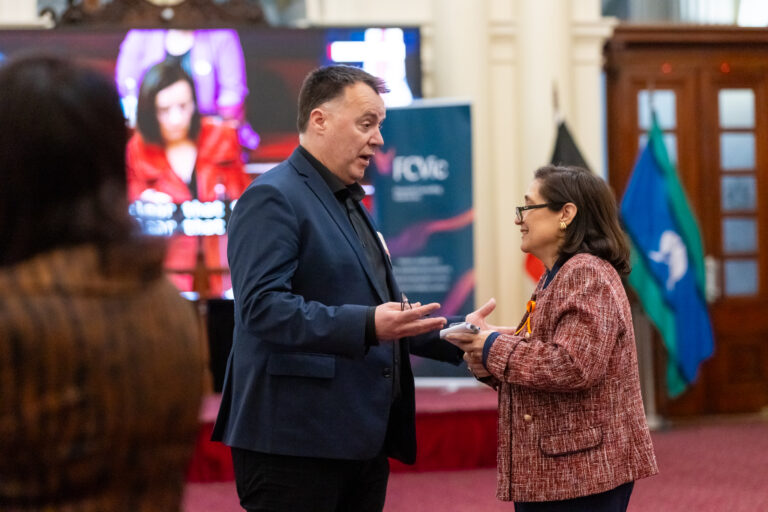 A man and a woman in conversation near the FCVic banner and Aboriginal flags.