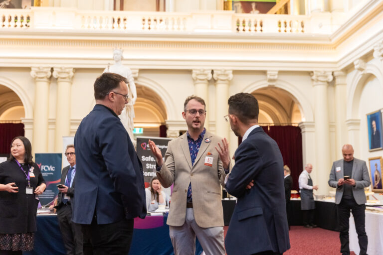 Three attendees in conversation in Queens Hall, with the Good Shepherd banner visible behind them.