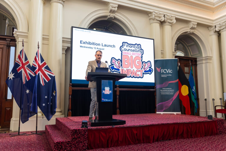 : FCVic CEO Zyl Hovenga-Wauchope addresses the Exhibition Launch on Wednesday 12 August, with flags and the FCVic banner on stage.