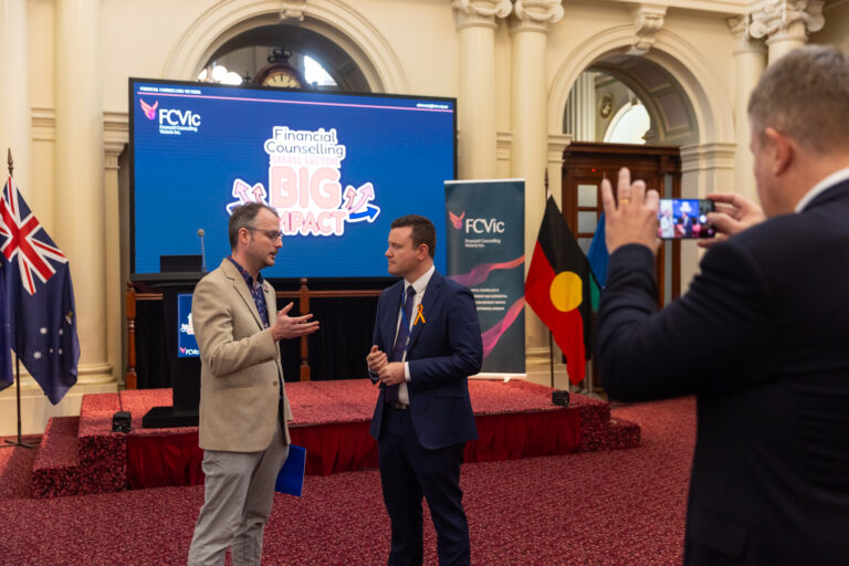FCVic CEO Zyl Hovenga-Wauchope and the Hon. Tim Richardson MP being photographed together on the stage area, flanked by the Australian and Aboriginal flags.