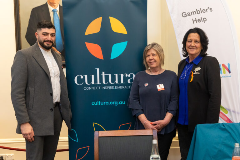 Chris Couzens MP stands with two others in front of the Cultura exhibition banner.