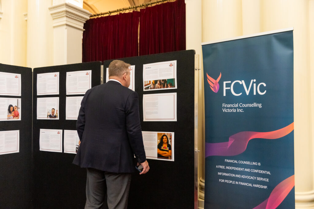 A man reads case study panels beside an FCVic banner describing financial counselling as a free, independent and confidential service.