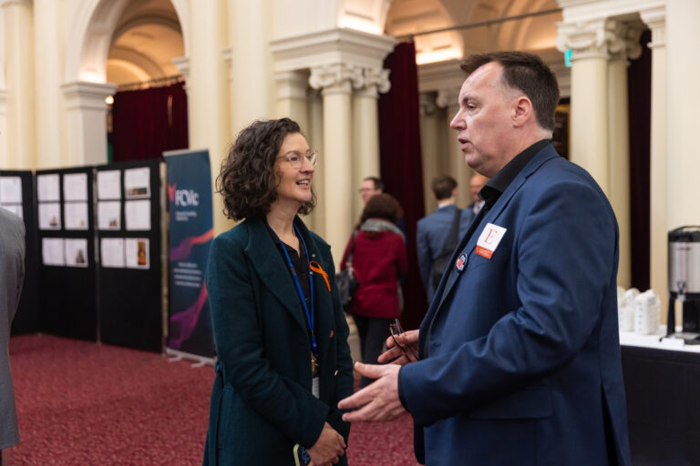 Ellen Sandell, Leader of the Victorian Greens, speaks with an attendee near the case study wall and FCVic banner.