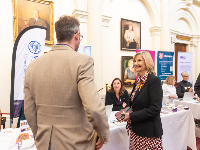 Kim O'Keefe MP speaks with the FCVic CEO near the Hume Community Housing and MELI exhibition banners.