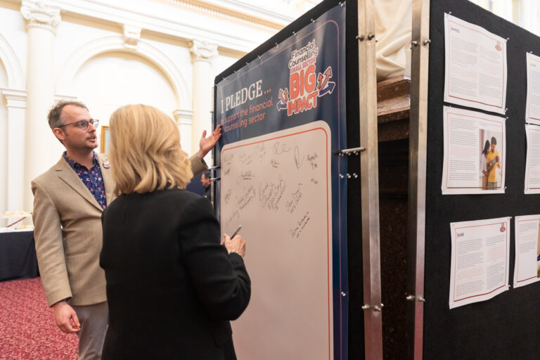Kim O'Keefe talks with an FCVic representative in front of the pledge wall and case study boards.
