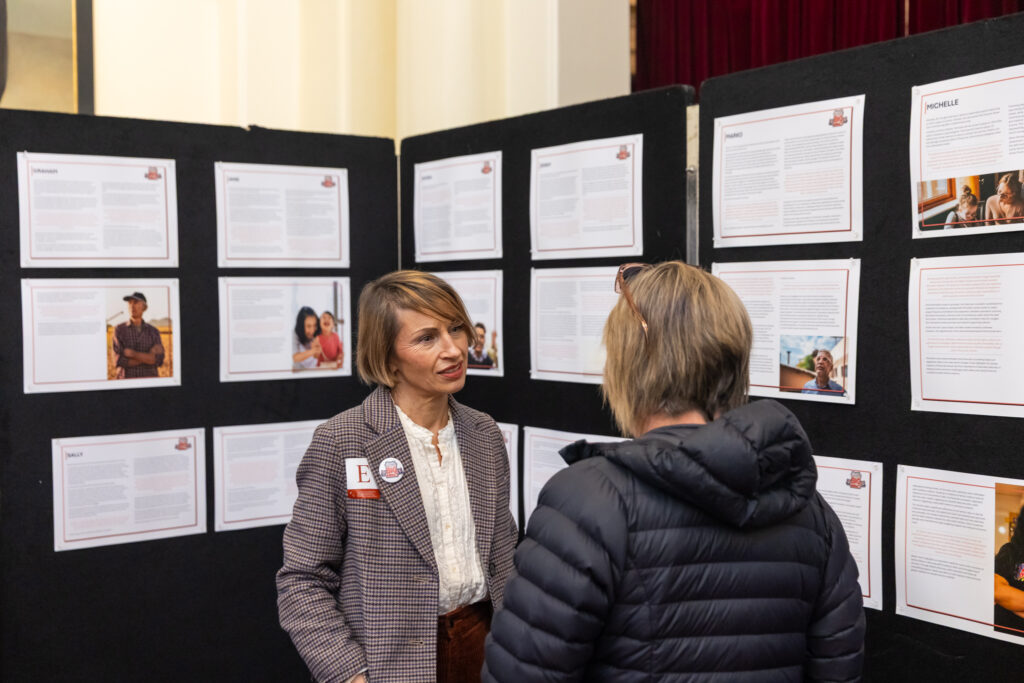 Two people in conversation in front of the case study display wall at the showcase.
