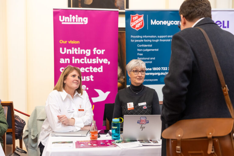 Two financial counsellors speak with a visitor at the Uniting and Salvation Army Moneycare exhibition booths.