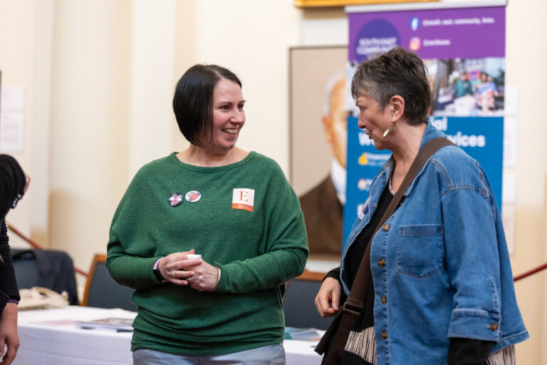 Two attendees share a laugh near the South East Community Links exhibition banner.