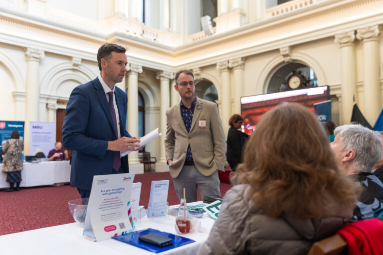 Tom McIntosh MP reviews a document at the Gambler's Help and BHN exhibition booth alongside an FCVic representative.