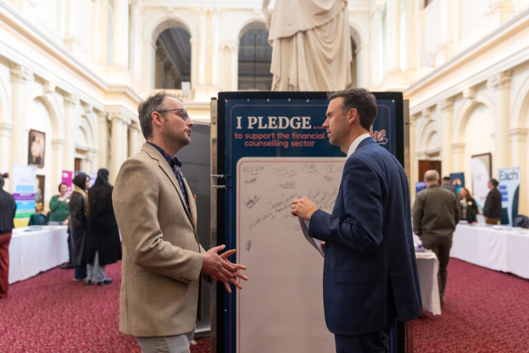 Tom McIntosh MP speaks with the FCVic CEO in front of the pledge wall.