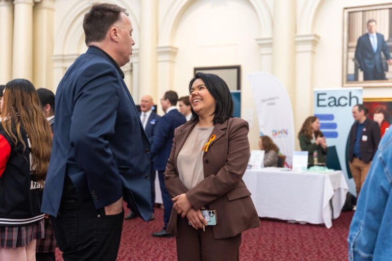 Eden Foster MP speaks with an attendee near the EACH and Gambler's Help exhibition banners.