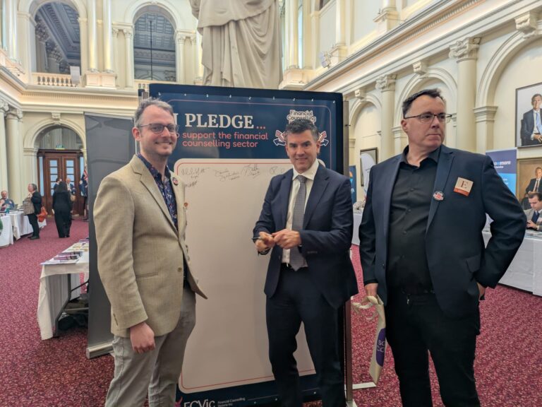 Brad Battin MP holds a pen to the "I Pledge" board while two attendees look on in Queen's Hall.