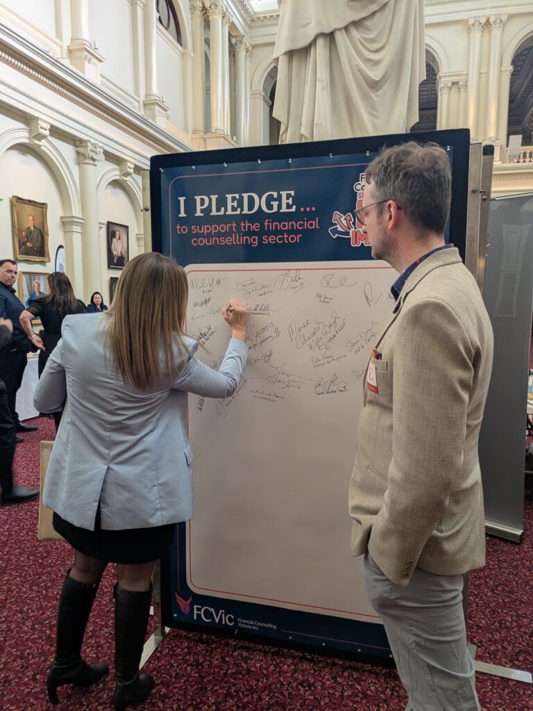Renee Heath MP signs the "I Pledge" board while an attendee looks on in Queen's Hall.