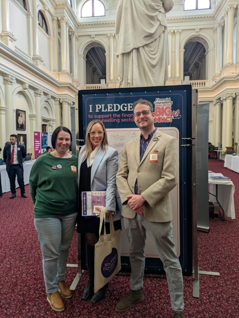 Renee Heath MP stands with two attendees beside the "I Pledge" board beneath a marble statue in Queen's Hall.