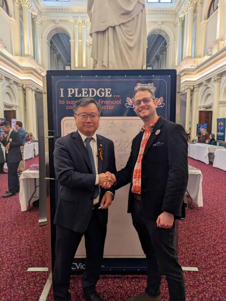 Meng Heang Tak MP shakes hands with FCVic's CEO in front of the "I Pledge" board in Queen's Hall.