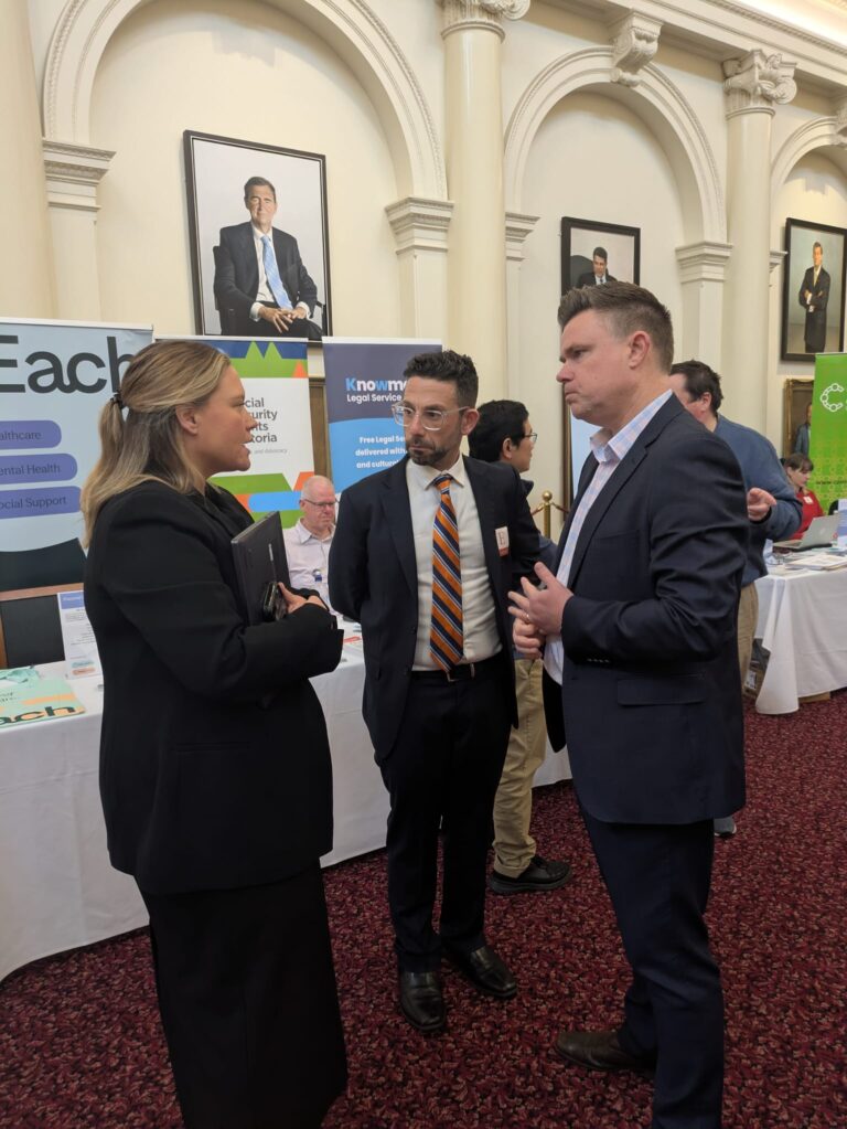 Ella George MP talks with two attendees beside exhibitor banners for Each and Knowmore Legal Service in Queen's Hall.