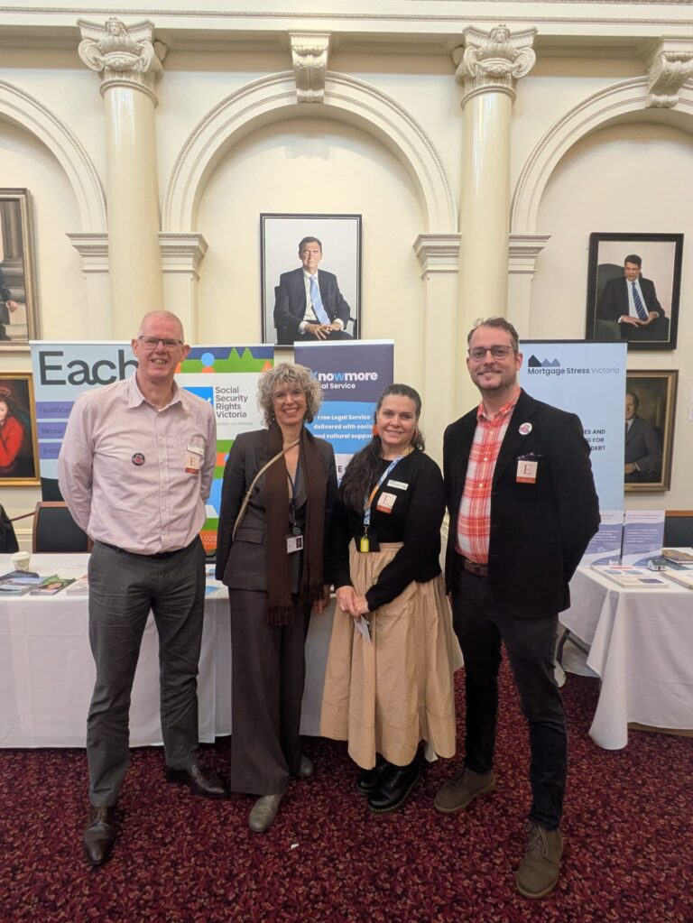 Nina Taylor MP poses with three attendees beneath historic portraits in Queen's Hall, with banners for Each, Social Security Rights Victoria, Knowmore Legal Service and Mortgage Stress Victoria visible behind.