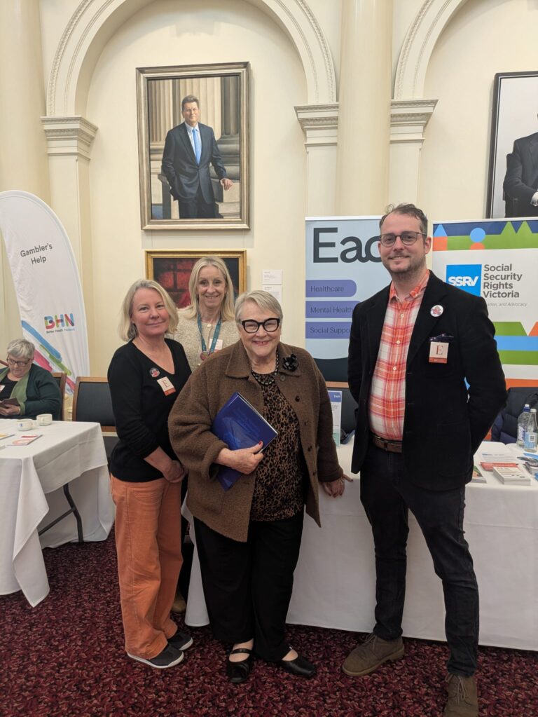 Bev McArthur MP poses with three attendees, including FCVic's CEO, beside exhibitor banners for Gambler's Help and Each in Queen's Hall.