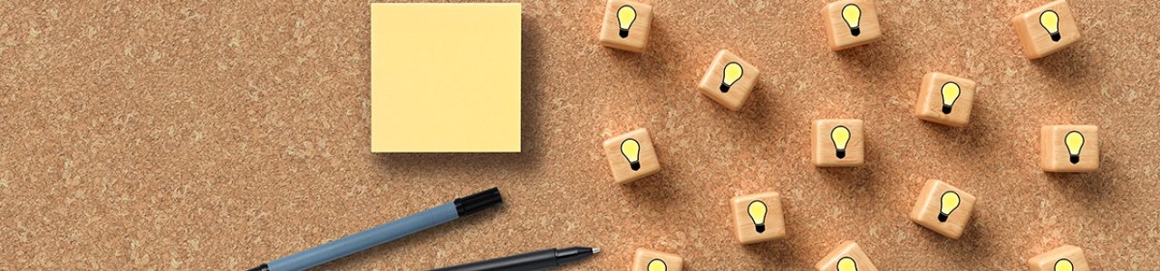 A cork board with lightbulb cubes, pen and sticky notes