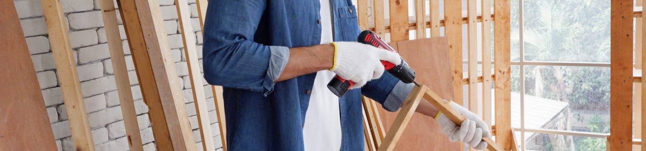 A carpenter uses an electric light to drill into a wooden plank.